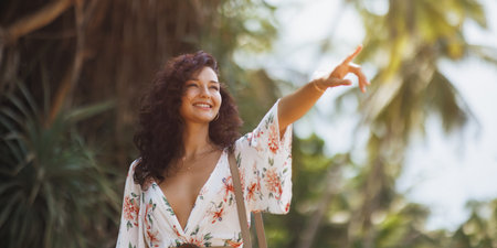 Smiling Woman in Floral Dress Pointing Towards Tropical Destinationの写真素材