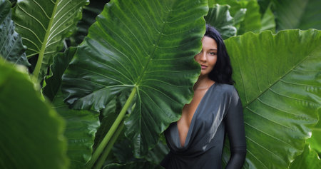 Tropical Woman Portrait Among Giant Elephant Ear Leaves In Lush Jungleの写真素材