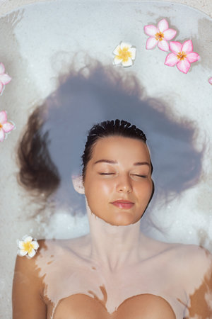 Relaxed Woman Floating In Spa Bath With Tropical Flowers Around