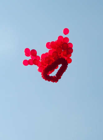 Red heart helium balloon floats against the blue skyの写真素材