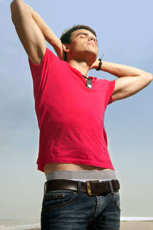 A young man in jeans and a shirt standing on the beachの写真素材