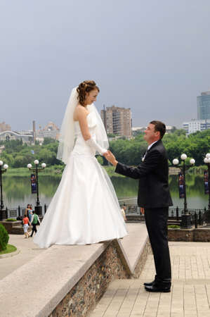 A married couple, bride and groom, about to kiss in sunshine on a beautiful waterfront cityのeditorial素材