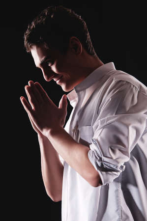 Young man praying in darkness with an enigmatic smileの写真素材