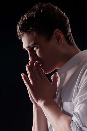 Young man praying in darkness with an enigmatic smileの写真素材
