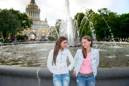 Two beautiful girls walking in the summer park end talking. Friends wearing stylish shirt and jeans , enjoying day off and have fun.の写真素材
