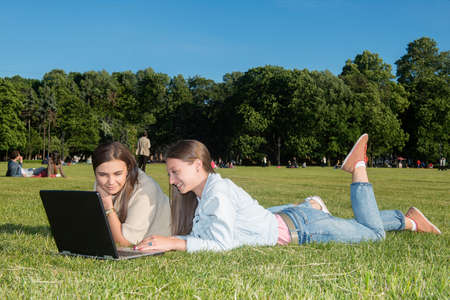 two friends with tablet computer sitting on the grass in the summer park. youth lifestyle