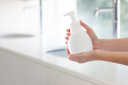 Hands holding soap pressed bottle at bathroom sink background.の写真素材