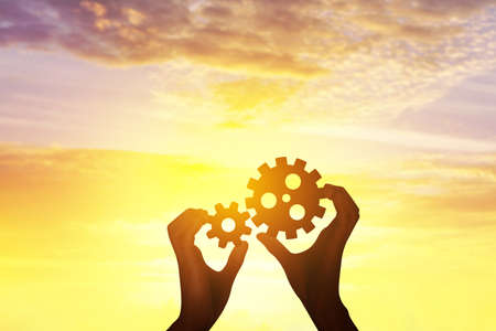 Silhouette hands holding gear from at sunlight background.
