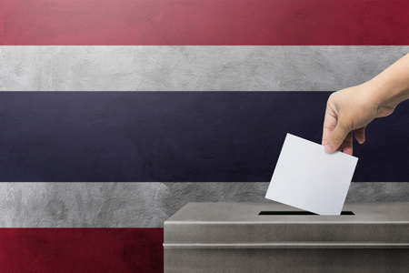 Hand holding ballot paper for election vote at thailand national flag on background. Thailand voting...
