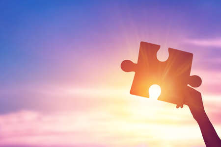 Silhouette of hands woman holding a jigsaw puzzle piece at sunsetsky for teamwork conceptの写真素材
