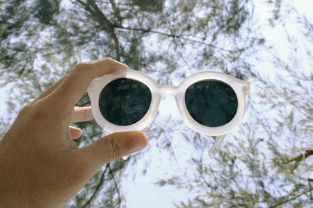 Hand holding sunglasses over the skyの写真素材
