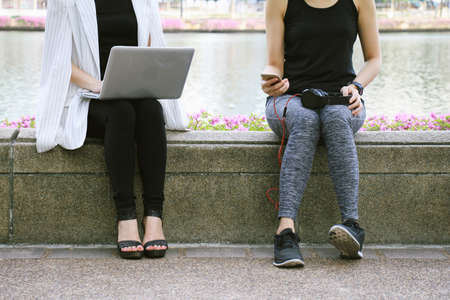 Business woman working on the laptop computer sitting near the relaxing sport woman in city park, Life balance concept, Workaholic and healthy lifestyle.の写真素材