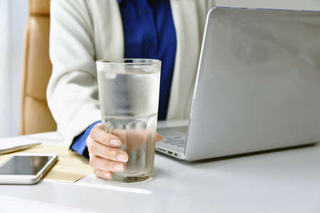 Business woman drinking fresh water while working at the office, A glass of drinking water on office desk, Drinking for good health concept.の写真素材