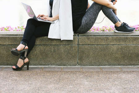 Business woman working on the laptop computer sitting near the relaxing sport woman in city park, Life balance concept, Workaholic and healthy lifestyle.の写真素材