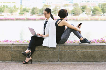 Business woman working on the laptop computer sitting near the relaxing sport woman in city park, Life balance concept, Workaholic and healthy lifestyle.の写真素材