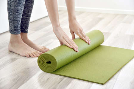 Woman folding yoga or fitness mat after working out at home, Home exercise workout.の写真素材