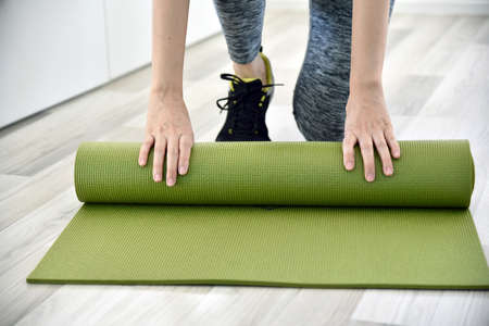 Woman folding yoga or fitness mat after working out at home, Home exercise workout.の写真素材
