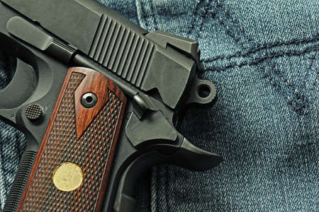 Semi-automatic handgun lying over a blue jeans, .45 pistol, Close-up cock and save.の写真素材