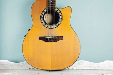 Old Acoustic guitar on white wooden table in front of blue background. (Vintage Style Color)