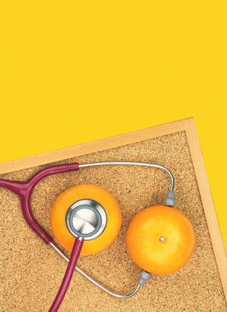 Stethoscope examining orange on a cork board. Medical equipment, Healthy food eating concept.の写真素材