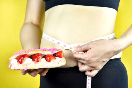 Diet failure, Overweight fat woman, Middle-aged woman with excessive belly, Fat woman holding sweet dessert and measuring tape.の写真素材