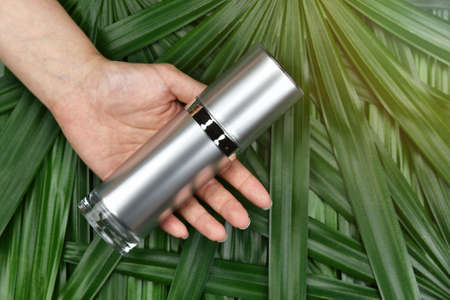 Natural skincare beauty product concept, Cosmetic bottle containers in hand on green herbal leaves background, Blank label for branding mock-up.の写真素材