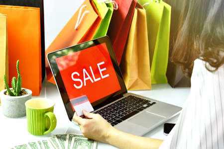 Online shopping, Shopaholic woman holding credit card, Sale promotion sign on laptop computer, E-business commercial concept.の写真素材