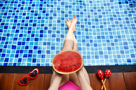 Beautiful bikini girl relaxing in swimming pool, Legs of woman in water, Fresh watermelon and summer...