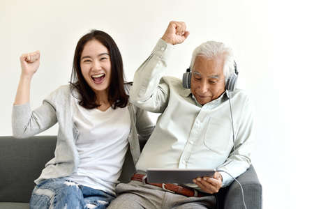 Happy family time, Smiling asian daughter and elderly father enjoy watching movie from laptop...