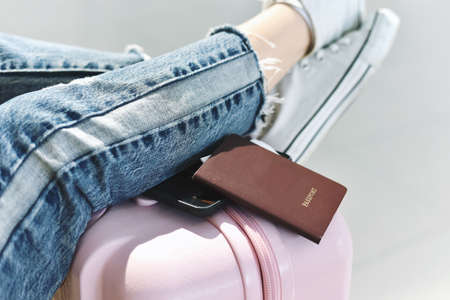 Traveler waiting for flight check-in at the airport, Passenger resting her feet on suitcase in...