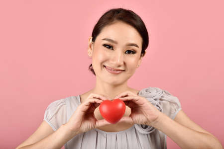 Gentle asian woman holding red heart, Happy smiling girl showing love sign to support and encourage, Cardiac health checkup.の写真素材