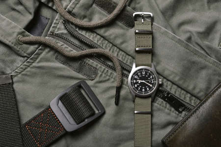 Vintage military watch with nato strap and tactical belt on army green background, Classic timepiece...