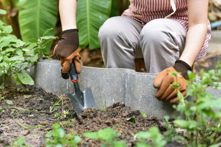 Gardener hand planting in backyard garden, Woman in gloves using hand shovel tool for seedling, Soil...