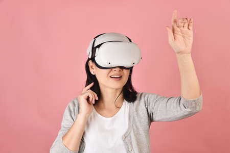 Asian woman using vr glasses, Hand grabbing something from virtual reality headset, Young woman having fun with new experience by vr technology, Studio shot.の写真素材