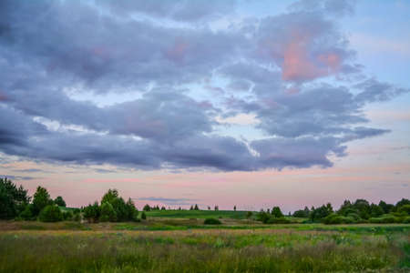 Summer evening landscape. Cloudy sky just before sunset, field, trees in the distance.の写真素材