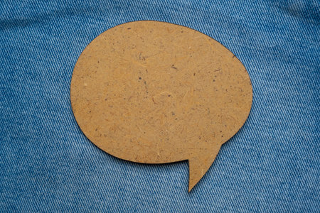 Wooden speech bubble balloon label on jeans background with shadow. Blank speech bubble on cloth...