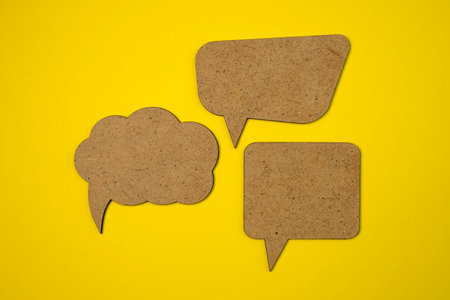 Brown handcrafted wooden blank speech bubbles on yellow background. Copy space.