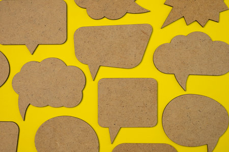 Wooden empty speech bubbles concept on yellow paper background with drop shadow. Copy space.