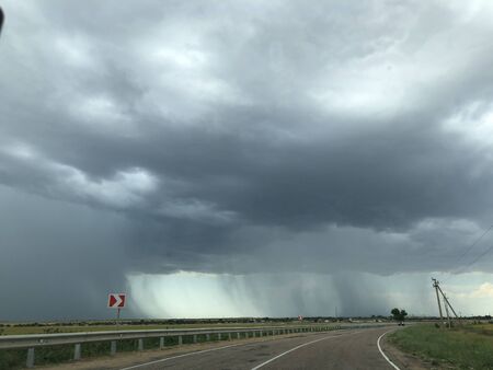 Rain from a cloud against the backdrop of the road and the sunny sky