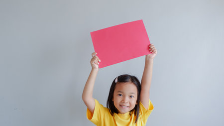 Portrait of a young asian little girl holding red paper blank sign over gray backgroundの写真素材
