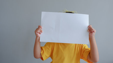 Portrait of a young asian little girl holding white paper blank sign over gray backgroundの写真素材