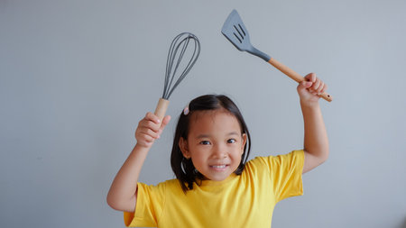 Little asian girl holding kitchen utensils on gray background.の写真素材