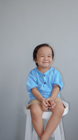 Little asian boy sitting on stool and smiling on grey backgroundの写真素材