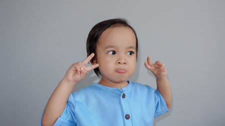 Little asian boy making a funny face with her fingers on grey backgroundの写真素材