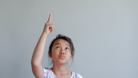 portrait of girl pointing up. isolated on light grey background.の写真素材