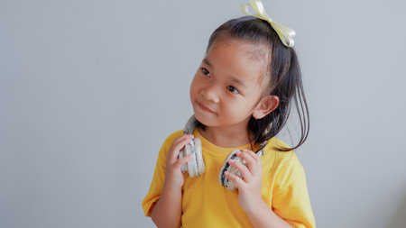 little asian girl wearing yellow tshirt and has a pair of headphones draped around her neck.の写真素材