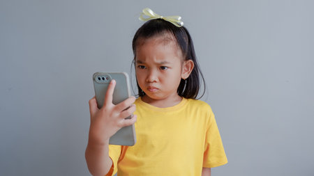 Little girl isolated on gray background hold smart phone look at screen make a call, play games, watch cartoons, parental control, children and modern tech usage conceptの写真素材