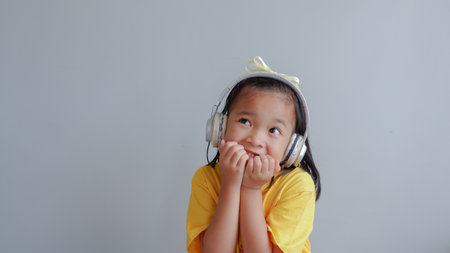 Happy asian little girl listen music with headphone on gray background.の写真素材