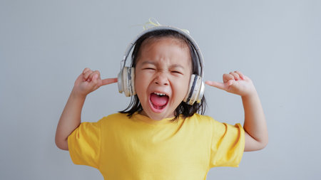 Cute child screaming using headphones at home. Little kid girl having fun at home. Childhood...