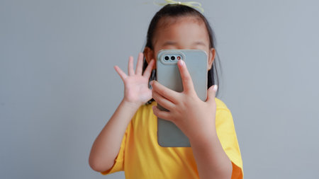 Little girl isolated on gray background hold smart phone look at screen make a call, play games, watch cartoons, parental control, children and modern tech usage conceptの写真素材